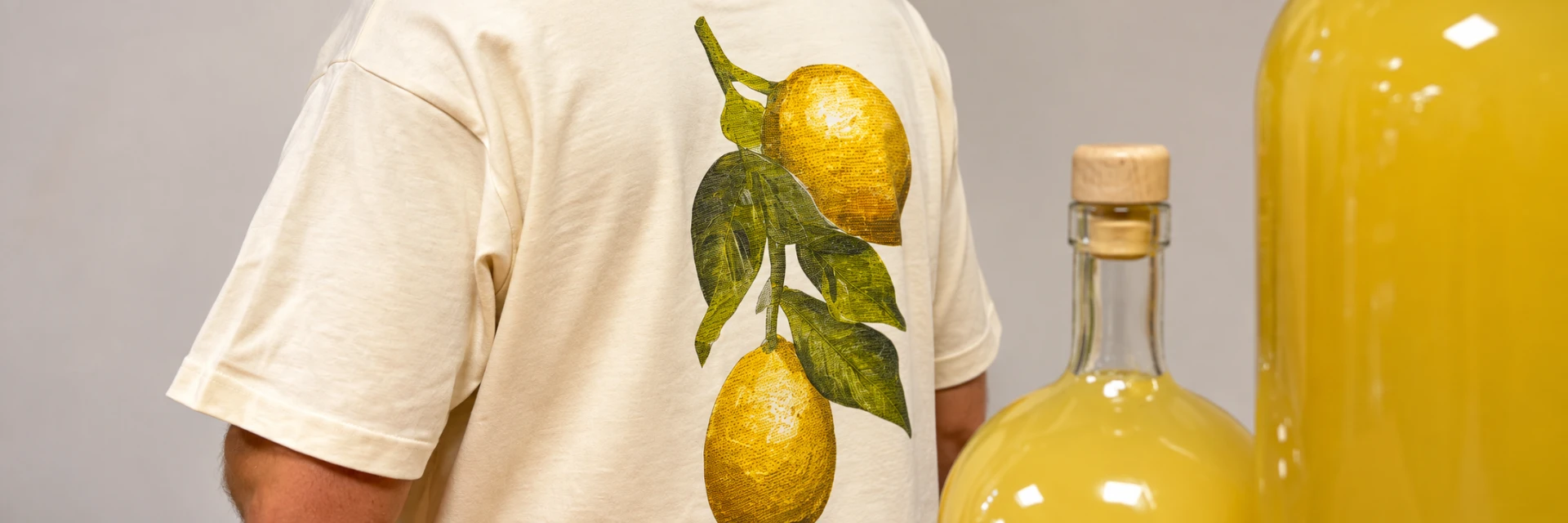 Rug van een natur t-shirt met geïllustreerde citroenen aan een tak, ernaast flessen limoncello